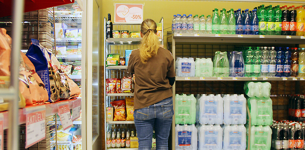Eine Mitarbeiterin mit langen blonden Haaren steht vor den Getränke-Regalen des SPAR Supermarktes Perspektive Handel in Villach und räumt diese ein.