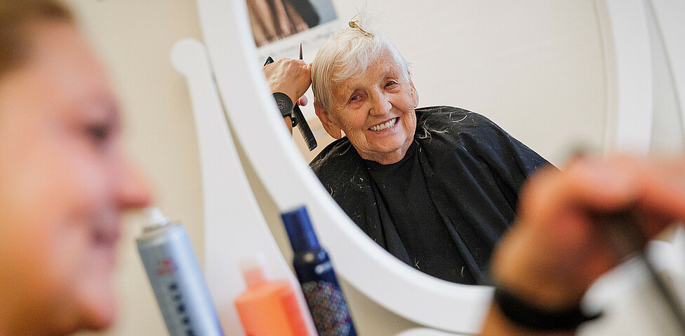Im Spiegel sieht man eine glückliche Dame, der gerade die Haare geschnitten werden.
