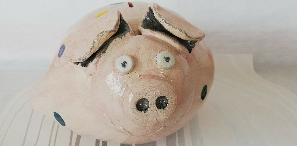 Ein rosa Sparschwein mit großen Augen und Schnauze aus Ton gefertigt.