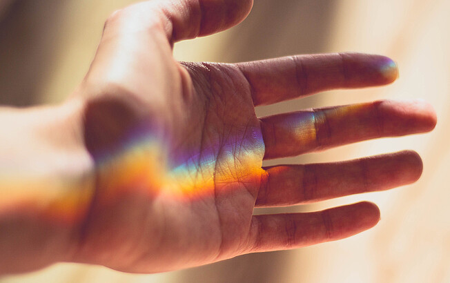Eine ausgestreckte Hand, die das Licht, dass sich in einen Regenbogen bricht, in der Hand hält.