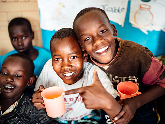 Eine Gruppe an Kindern in Afrika mit bunten Trinkbechern in der Hand lächeln.