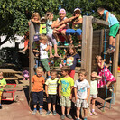 Kinder des Pfarrkindergarten Annabichl stehen vor dem Spielturm im Garten und lächeln in die Kamera.