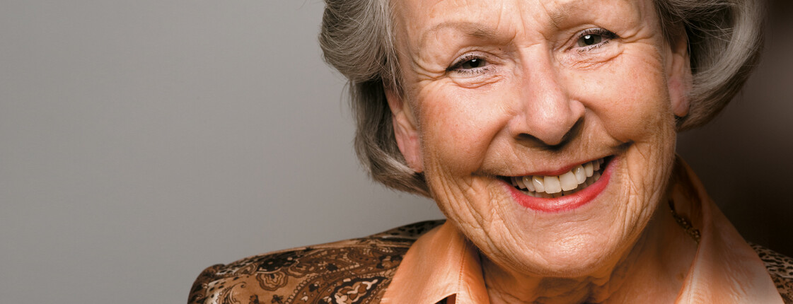 Eine ältere Dame, die schick gekleidet ist, lächelt in die Kamera.