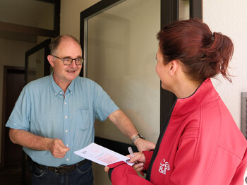 Zwei Personen am Hauseingang, eine mit roter Caritas-Jacke, übergibt Spendeninfos an Bewohner.