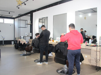 Ein Barbershop mit zwei Friseuren die sich um Kunden kümmern, die auf Stühlen vor großen Spiegel sitzen.