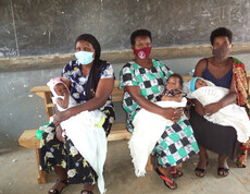 Drei Mütter sitzen mit ihren Kindern im Arm auf einer Bank und warten.