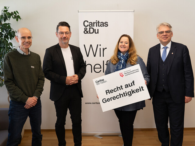 Caritas-Jurist Peter Leitner, Caritasdirektor Ernst Sandriesser, Kammeramtsdirektorin Susanne Laggner-Primosch und Rechtsanwaltskammerpräsident Bernhard Fink stehen vor einem Caritas-Rollup und halten ein Schild Recht auf Gerechtigkeit in der Hand.  