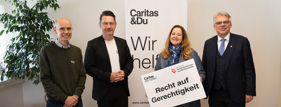 Caritas-Jurist Peter Leitner, Caritasdirektor Ernst Sandriesser, Kammeramtsdirektorin Susanne Laggner-Primosch und Rechtsanwaltskammerpräsident Bernhard Fink stehen vor einem Caritas-Rollup und halten ein Schild Recht auf Gerechtigkeit in der Hand.  
