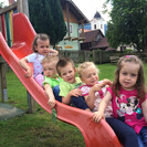 Kinder der Pfarrkindertagesstätte Liliput sitzen auf der Rutsche im Garten und lächeln in die Kamera.