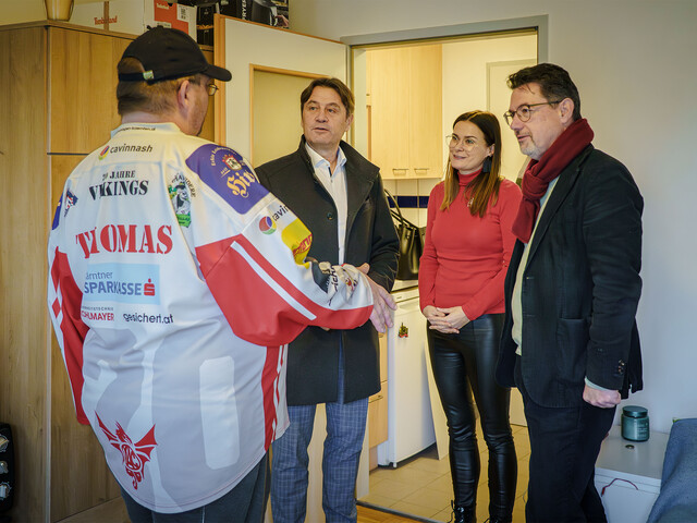 Drei Personen sprechen in einer kleinen Wohnung mit einem Unterstützten im Caritas-Kontext der Wohnsicherung.