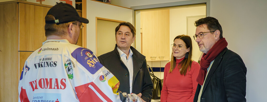 Drei Personen sprechen in einer kleinen Wohnung mit einem Unterstützten im Caritas-Kontext der Wohnsicherung.