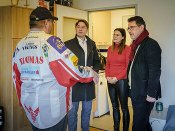 Drei Personen sprechen in einer kleinen Wohnung mit einem Unterstützten im Caritas-Kontext der Wohnsicherung.