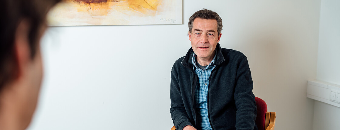 Ein Mann sitzt vor einem Berater der Männerberatung, zwischen ihnen befindet sich ein kleiner Tisch.