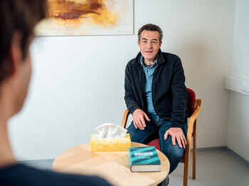 Ein Mann sitzt vor einem Berater der Männerberatung, zwischen ihnen befindet sich ein kleiner Tisch.