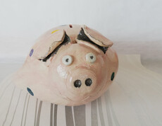 Ein rosa Sparschwein mit großen Augen und Schnauze aus Ton gefertigt.