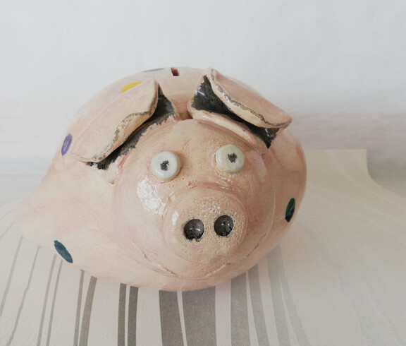 Ein rosa Sparschwein mit großen Augen und Schnauze aus Ton gefertigt.