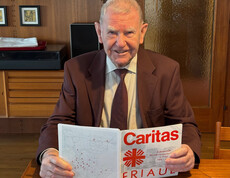 Eine Person sitzt an einem Tisch und liest eine Broschüre mit dem Titel „Caritas Friaul“ zur Erdbebenhilfe 1976.