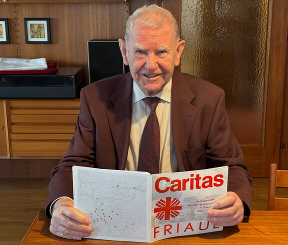 Eine Person sitzt an einem Tisch und liest eine Broschüre mit dem Titel „Caritas Friaul“ zur Erdbebenhilfe 1976.