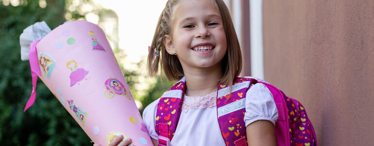Ein Mädchen hält eine rosa Schultüte in der Hand und trägt einen pinken Rucksack.