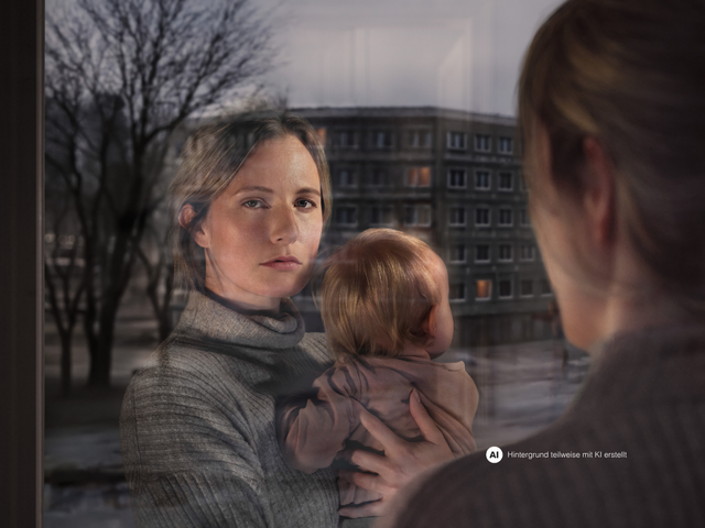 Eine Frau mit Kind am Arm schaut aus dem Fenster. Ihr Gesicht spiegelt sich im Fensterglas wider. Vor dem Fenster ist eine Wohngegend erkennbar.