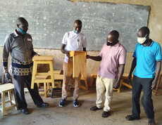 Jugendliche, die zum Tischler ausgebildet werden zeigen stolz zwei selbstgebaute Hocker den Projektverantwortlichen.