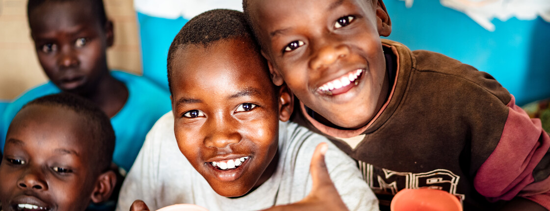 Eine Gruppe an Kindern in Afrika mit bunten Trinkbechern in der Hand lächeln.