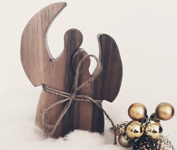 Zwei Engel aus Holz sind auf Watte und mit goldenen Kugeln verziert vor einem weißen Hintergrund drapiert.