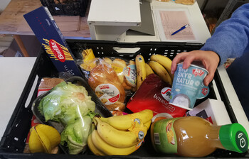 Ein Korb voll mit Lebensmitteln, darunter Bananen Saft, Joghurt Salar und Nudeln.