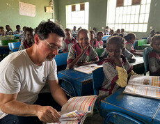 Schüler*innen sitzen im Klassenzimmer. Ernst Sandriesser sieht gemeinsam mit einer Schülerin in ein Schulbuch.