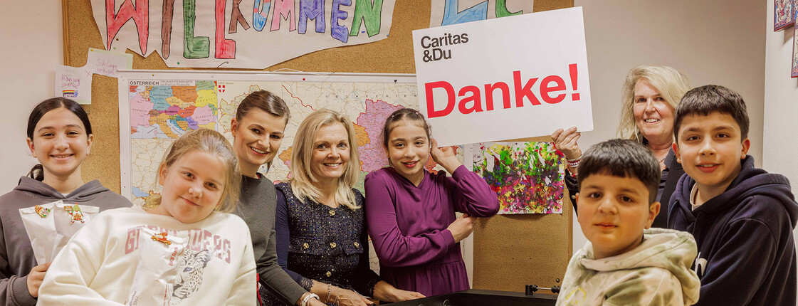 Zwei Bankmitarbeitende stehen mit den Kindern des Lerncafé Spittals an einem Tischfussballtisch. Ein Mädchen hält ein Danke-Schild in die Höhe.