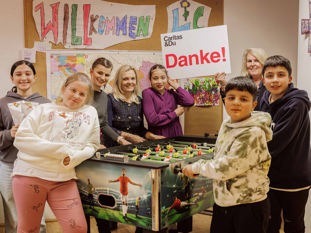Zwei Bankmitarbeitende stehen mit den Kindern des Lerncafé Spittals an einem Tischfussballtisch. Ein Mädchen hält ein Danke-Schild in die Höhe.