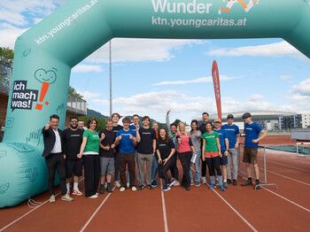 Gruppe von youngCaritas-Mitarbeitenden und Freiwilligen unter dem LaufWunder-Startbogen auf einer Laufbahn.
