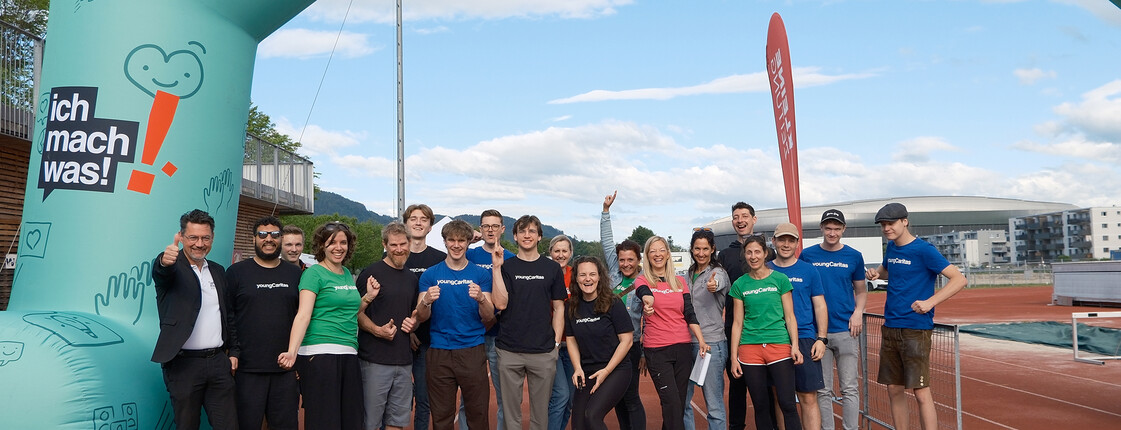 Gruppe von youngCaritas-Mitarbeitenden und Freiwilligen unter dem LaufWunder-Startbogen auf einer Laufbahn.