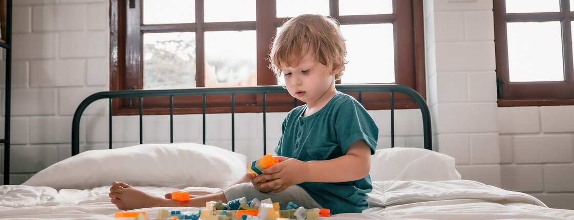Ein Kind sitzt mit Spielzeug auf einem Bett.