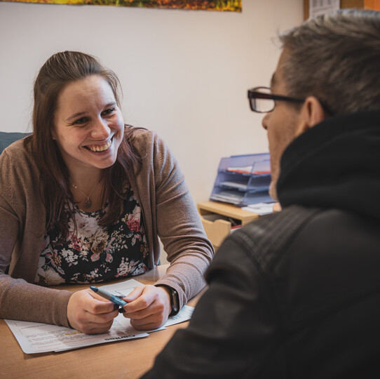 Frau lächelt Mann bei Gespräch am Tisch in einem Büro an