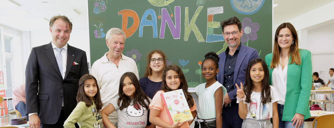 Kinder und Erwachsene vor einer Tafel mit „DANKE“ bei Spendenübergabe im Caritas-Lerncafe.
