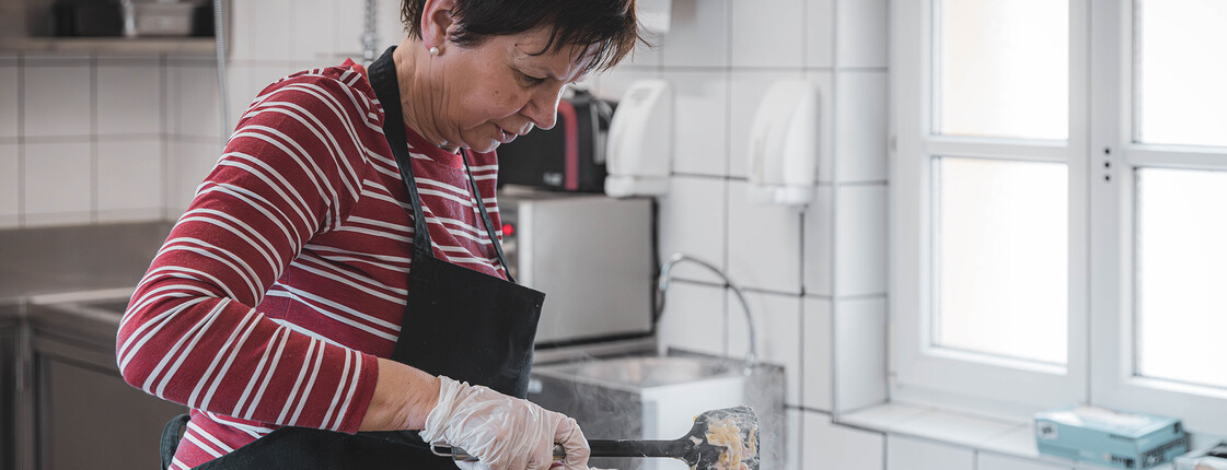 Eine Frau serviert in der Küche des Eggerheims eine warme Mahlzeit – Hilfe, die satt und würdevoll macht.