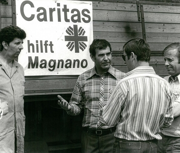 Mehrere Personen stehen vor einem Lkw mit der Aufschrift „Caritas hilft Magnano“ und besprechen Hilfsmaßnahmen vor Ort.