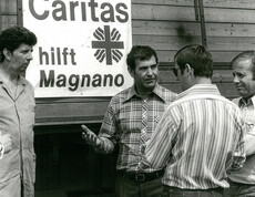 Mehrere Personen stehen vor einem Lkw mit der Aufschrift „Caritas hilft Magnano“ und besprechen Hilfsmaßnahmen vor Ort.