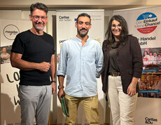 Ein Teilnehmer steht mit Caritasdirektor und Projektleiterin bei einer Zertifikatsverleihung vor Roll-ups von Caritas und Perspektive Handel.
