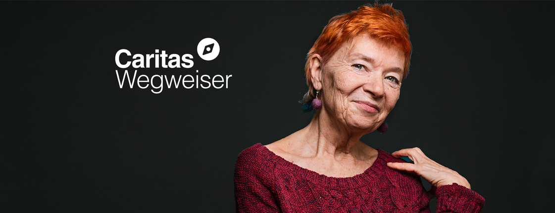 Caritas Wegweiser - Hilfe suchen. Hilfe finden. Das Porträt einer Frau ist zu sehen auf schwarzem Hintergrund. Es ist eine ältere Dame die lächelt, sie hat einen rothaarigen Kurzhaarschnitt. Links oben das Logo vom Caritas Wegweiser.