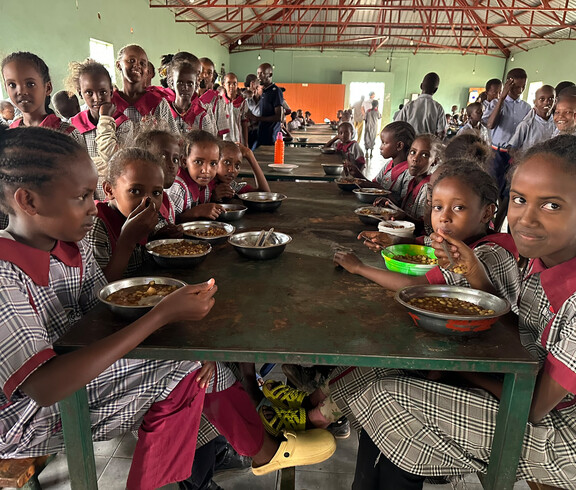 Mädchen in Schuluniform essen ihr Mittagessen an der Tiigo School in Kenia.