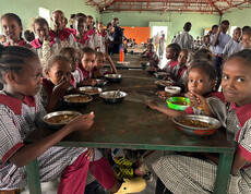 Mädchen in Schuluniform essen ihr Mittagessen an der Tiigo School in Kenia.
