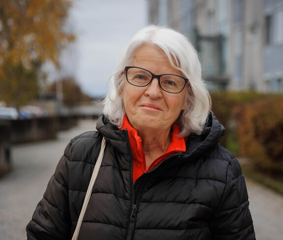 Margit Müller steht draußen vor Gebäuden und Herbstbäumen in Klagenfurt