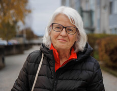 Margit Müller steht draußen vor Gebäuden und Herbstbäumen in Klagenfurt