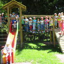 Kinder des Pfarrkindergarten Winklern stehen vor dem Spielturm im Garten und lächeln in die Kamera.