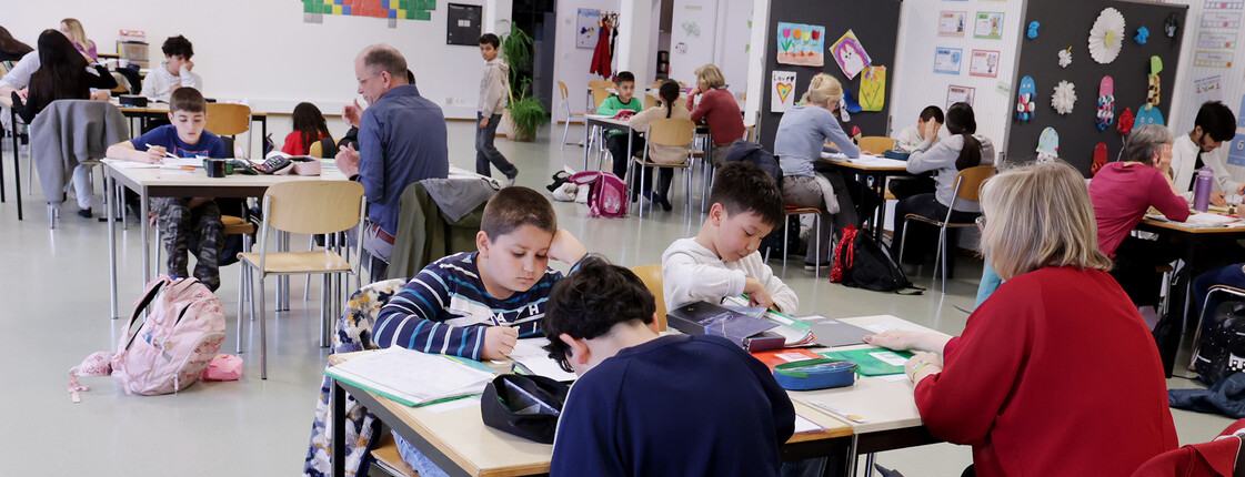 Kinder und Freiwillige arbeiten im Lerncafé an Hausübungen und Schulaufgaben in einem Gruppenraum.