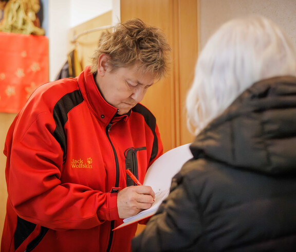 Person trägt Daten in eine Spendenliste ein, Margit Müller steht daneben.