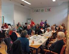 Viele Bewohner*innen sitzen an Tischen im Saal mit Weihnachtsdekoration und Getränken.