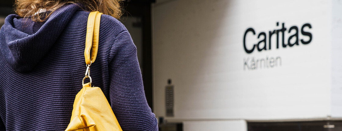 Person mit gelber Tasche steht vor Eingang der Caritas Kärnten und sucht Unterstützung.